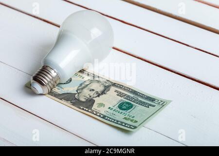 led-Lampe mit Geld liegt auf einem weißen Holztisch von Bord. Stockfoto