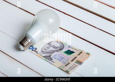 led-Lampe mit Geld liegt auf einem weißen Holztisch von Bord. Stockfoto