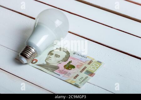 led-Lampe mit Geld liegt auf einem weißen Holztisch von Bord. Stockfoto