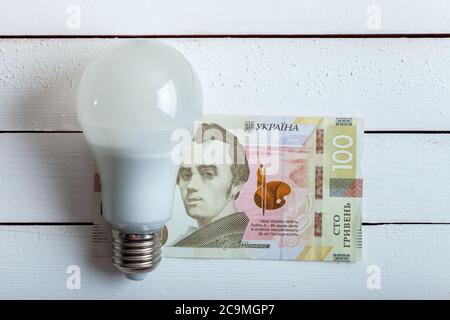 led-Lampe mit Geld liegt auf einem weißen Holztisch von Bord. Stockfoto