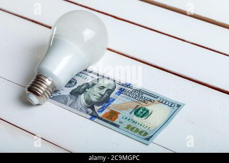 led-Lampe mit Geld liegt auf einem weißen Holztisch von Bord. Stockfoto