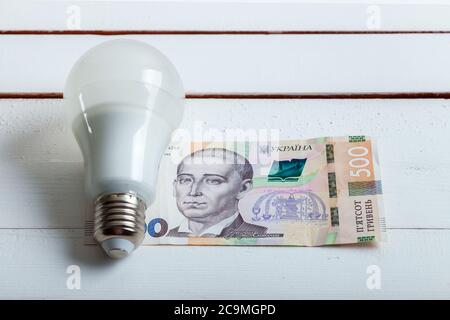 led-Lampe mit Geld liegt auf einem weißen Holztisch von Bord. Stockfoto