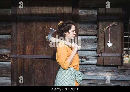 Mädchen mit einer Axt in der Nähe eines Holzhauses in den Bergen Stockfoto