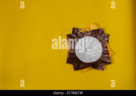 Drei quadratische Stücke von farbigen Folie auf gelb. Folienstücke braun und gelb mit einem weißen Kreis. Abstrakter Hintergrund. Flach liegend. Stockfoto