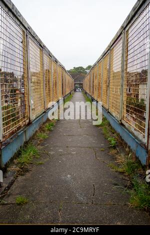 Ein allgemeiner Blick auf eine schmale Eisenbahnfußbrücke, die verwittert ist, rostig mit einigen Graffiti, die Perspektive und führende Linien zeigen. Stockfoto