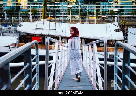 Eine rothaarige brasilianerin in ihren Zwanzigern betritt ein großes Boot, das im Geschäftsviertel von Puerto Madero geparkt ist, blickt zurück zur Kamera und lächelt. Stockfoto