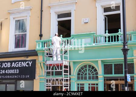 Maler und Dekorateur Mann arbeitet draußen auf Gerüsten an einem heißen sonnigen Sommertag im juli, hastings, East sussex, großbritannien Stockfoto