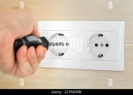 Die Hand des Maurers des Elektrikers hält den Schraubendreher und machen die Installation der Steckdose auf 220 in auf der keramischen Oberfläche. Stockfoto
