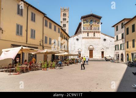 Lucca, Toskana, Italien - 3. Juli 2019: San Frediano Platz mit Menschen genießen die Outdoor-Bar und Blick auf die Basilika von San Frediano in der Altstadt L Stockfoto