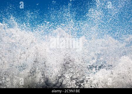 Spray von Wellen, die über einen Felsen krachen, mit einem blauen Himmel dahinter Stockfoto