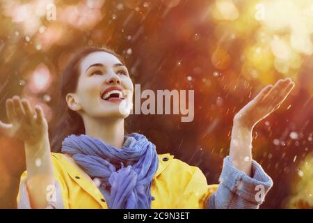 Glückliche schöne junge Frau unter der Herbstdusche. Mädchen trägt gelben Regenmantel und genießen Niederschläge. Stockfoto