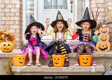 Frohe Halloween! Drei süße kleine lachende Mädchen in Hexen-Kostümen kommen zum Haus für Süßigkeiten. Stockfoto