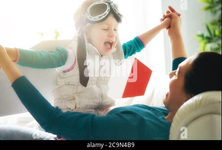 Glückliche Familie hat Spaß zu Hause. Mutter und ihr Kind spielen zusammen. Mädchen in Pilotenkostüm. Stockfoto