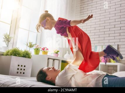 Mutter und ihr Mädchen spielen zusammen. Mädchen in einem Superman's Kostüm. Das Kind hat Spaß und springt auf dem Bett. Stockfoto