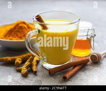 Gelber Kurkuma Latte Drink. Goldene Milch mit Zimt, Kurkuma, Ingwer und Honig auf grauem Betongrund. Stockfoto