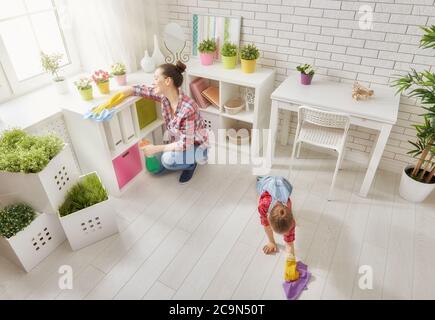 Glückliche Familie putzt das Zimmer. Mutter und Tochter machen die Reinigung im Haus. Eine junge Frau und ein kleines Mädchen entstauben. Stockfoto