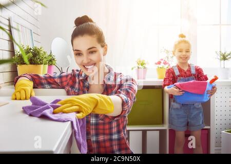 Glückliche Familie putzt das Zimmer. Mutter und Tochter machen die Reinigung im Haus. Eine junge Frau und ein kleines Mädchen entstauben. Stockfoto