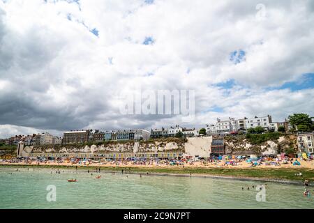 Blick vom Meer auf Broadstairs Strand überfüllt mit Menschen Sonnenbaden im Sommer mit der Stadt auf der Klippe dahinter. Himmel gefüllt mit dicken Wolken. Stockfoto