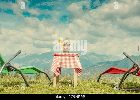 Stillleben der Arosa Berge in der Schweiz mit kleinem Tisch und karierter Tischdecke. Eine Vase mit Blumen steht auf dem Tisch Stockfoto