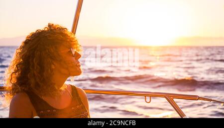 Porträt einer schönen erwachsenen kaukasischen Frau, die den Sonnenuntergang auf einem Boot genießt - Reise- und Freiheitskonzept für junge Menschen - Natur im Freien mit blauem o Stockfoto