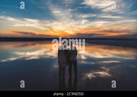 Portrait, Silhouette des glücklichen Paares beobachten die bunten hellen Sonnenuntergang stehen in großen See und küssen, Reflexion im Wasser, Hände halten Stockfoto