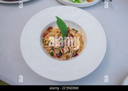Blick von oben auf Spaghetti mit Speck Chili oder 'Spaghetti Pad Prik Bacon', italienische Fusion-Küche im Thai-Stil Serve mit weißem Gericht auf dem Holztisch. Whi Stockfoto