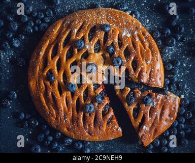 Draufsicht auf einen rund geschnittenen hausgemachten Kuchen mit Heidelbeerfüllung, der zwischen reifen Blaubeeren steht. Hausgemachter Kuchen. Stockfoto