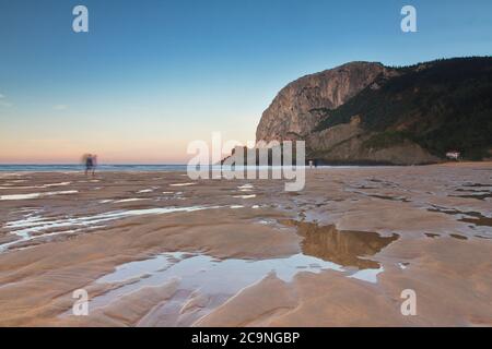 Ibarrangelu, Bizkaia/Baskenland; 26. September 2015. Leute, die bei Ebbe am Strand von Laga bei Sonnenuntergang spazieren gehen. Stockfoto