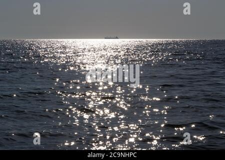 Eine Silhouette des Frachtschiffes weit entfernt im Meer an sonnigen Tagen Stockfoto