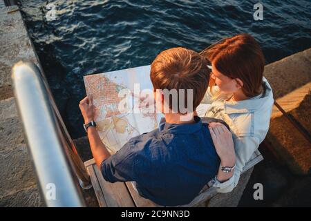 Nahaufnahme eines glücklichen jungen Paares auf der Holzterrasse am Hafen mit einer Karte in den Händen, Reisekonzept Stockfoto