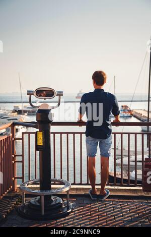 ODESSA, UKRAINE - 06. AUGUST 2015: Junger Mann, der sich vom Aussichtspunkt Hi Spy Viewing Machine am Hafen freut, Rückansicht Stockfoto