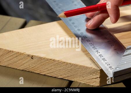 Ein Nahaufnahme Porträt von jemandem mit einem Edelstahl L-Quadrat oder Haken zu messen und zeichnen eine perfekt senkrechte Linie auf einem Holzbrett. Die Perso Stockfoto