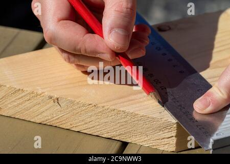 Ein Nahaufnahme Porträt eines Mannes mit einem Bleistift und einem Edelstahl L-Quadrat oder Haken, um eine senkrechte Linie über eine Holzdiele zeichnen. Stockfoto