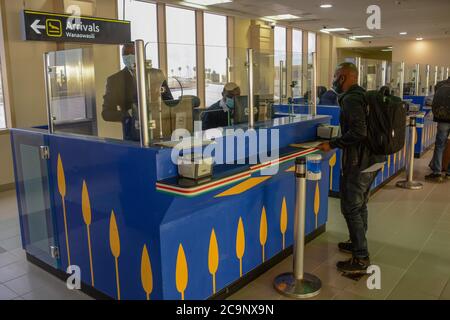 Ein Einwanderungsbeamter am Jomo Kenyatta International Airport in Nairobi räumt einen Passagier mit Gesichtsbemaler, der aus Kigali, Ruanda, ins Land gekommen war, frei. Kenya Airways hat die internationalen Flüge nach der Lockerung der Reisebeschränkungen durch Präsident Uhuru Kenyatta wieder aufgenommen. Die Flüge wurden während des Ausbruchs der Coronavirus-Pandemie im Land gestoppt. Stockfoto