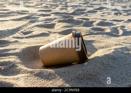 Einweg-Kaffeetasse am Strand. Naturschutz und Umweltverschmutzung Konzept. Stockfoto