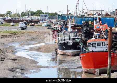 Fischereiflotte bei Ebbe in Old Leigh, Leigh on Sea, Essex, Großbritannien. Person, die bei einem großen Fischerboot steht, um die Waage zu erhalten. Fischerboote, Schiffe. Herzmuschel Stockfoto