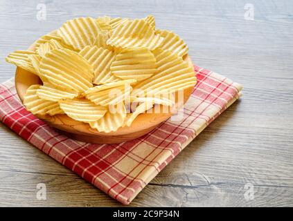 Gewellte goldene Kartoffelchips in einer Holzschale auf rustikalem Holztisch. Stockfoto