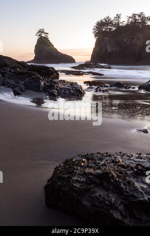 Die Sonne geht am Secret Beach an der südlichen Küste von Oregon bei Sonnenuntergang unter, mit seinen vielen Inselchen, die mit immergrünen Bäumen und verschwommenen Wellen übersät sind Stockfoto