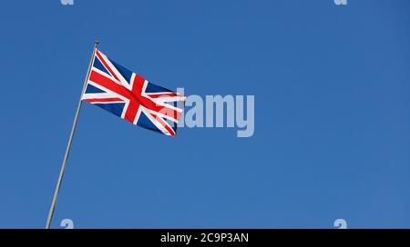 Die britische Flagge schwenkt auf einem Fahnenmast gegen einen klaren blauen Himmel. Stockfoto
