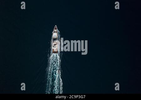 Top Luftbild auf die Luxus-Kreuzfahrt-Yacht mit einer Welle Spuren auf der dunkelblauen Farbe Ozeanoberfläche. Um die Welt reisen Menschen auf dem Meer und Trans Stockfoto