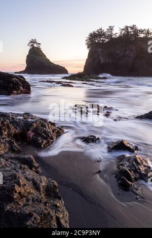 Die Sonne geht am Secret Beach an der südlichen Küste von Oregon bei Sonnenuntergang unter, mit seinen vielen Inselchen, die mit immergrünen Bäumen und verschwommenen Wellen übersät sind Stockfoto