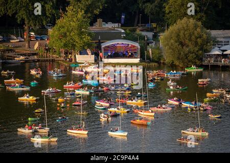 01. August 2020, Bayern, Nürnberg: Die Staatsphilharmonie (h, M) spielt auf der Seestufe auf dem Großen Dutzendteich ein Konzert vor Zuschauern, die das Konzert auf eigenen Booten verfolgen. Aufgrund der musikalischen Veranstaltungen Bardentreffen, Klassik Open Air und Stars in Luitpoldhain, die aufgrund von Corona abgesagt wurden, hat das Projektbüro im Kulturbereich der Stadt Nürnberg drei verschiedene Konzerte mit einem Open-Air-Konzertwochenende am Ufer des Dutzendteichs organisiert. Das einzigartige Angebot soll als Brückenhilfe und Experiment in einem dienen. Das Publikum wird ihr o mitbringen müssen Stockfoto