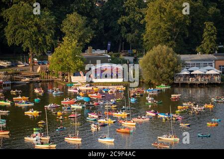 01. August 2020, Bayern, Nürnberg: Die Staatsphilharmonie (h, M) spielt auf der Seestufe auf dem Großen Dutzendteich ein Konzert vor Zuschauern, die das Konzert auf eigenen Booten verfolgen. Aufgrund der musikalischen Veranstaltungen Bardentreffen, Klassik Open Air und Stars in Luitpoldhain, die aufgrund von Corona abgesagt wurden, hat das Projektbüro im Kulturbereich der Stadt Nürnberg drei verschiedene Konzerte mit einem Open-Air-Konzertwochenende am Ufer des Dutzendteichs organisiert. Das einzigartige Angebot soll als Brückenhilfe und Experiment in einem dienen. Das Publikum wird ihr o mitbringen müssen Stockfoto