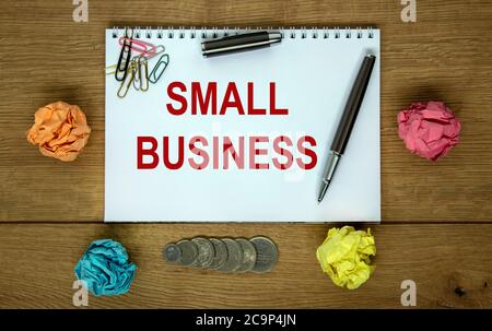Weiße Note mit Aufschrift "kleines Geschäft" auf schönem Holztisch, farbigem Papier, Metallstift. Geschäftskonzept. Stockfoto
