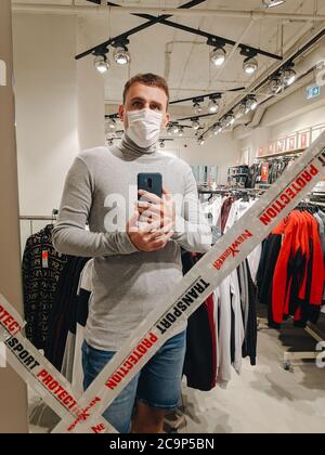 Budva, Montenegro - 01. august 2020: Ein Mann mit einer medizinischen Maske nimmt ein Selfie auf seinem Telefon im Spiegel der geschlossenen Umkleideräume, in Verbindung mit Stockfoto