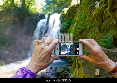 Eine Frau fotografiert mit ihrem iPhone einen Wasserfall in den Cascade Mountains im Zentrum von Oregon. Stockfoto