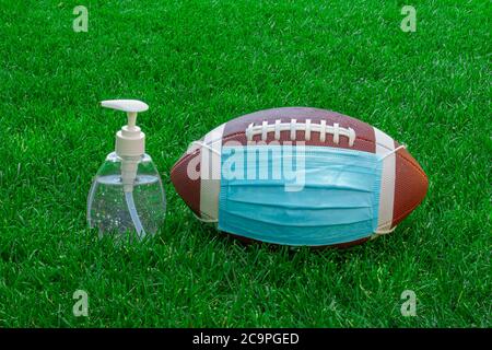 Ein American Football mit Gesichtsmask und Händedesinfektionsmittel auf dem Feld mit grünem Gras. Konzept Fußball während Pandemie Stockfoto