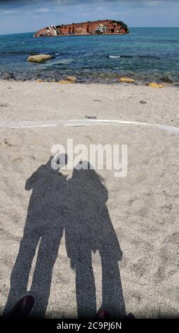 Schattenbilder von Mann und Frau auf Strandsand und altes rostig zerstörtes Schiff im Wasser auf verschwommenem Hintergrund Stockfoto