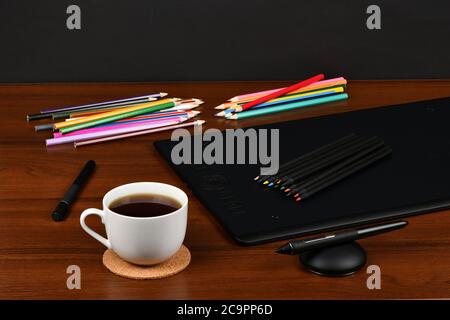 Professionelles Grafiktablett mit Kaffeetasse, digitalisierte und mehrfarbige Stifte auf Holztisch. Hochauflösendes Foto. Volle Schärfentiefe. Tabelle concep Stockfoto