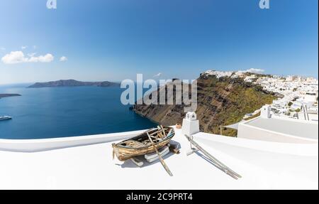 Altes Holzboot auf den weißen Dächern von Caldera in Santorini, Griechenland. Erstaunliche Sommerlandschaft, Reiseabenteuer, Meerblick über weiße Architektur. Stockfoto